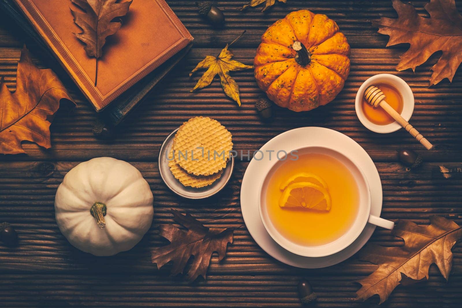 Hot lemon tea with fall foliage and pumpkins, books and cookies on wooden background