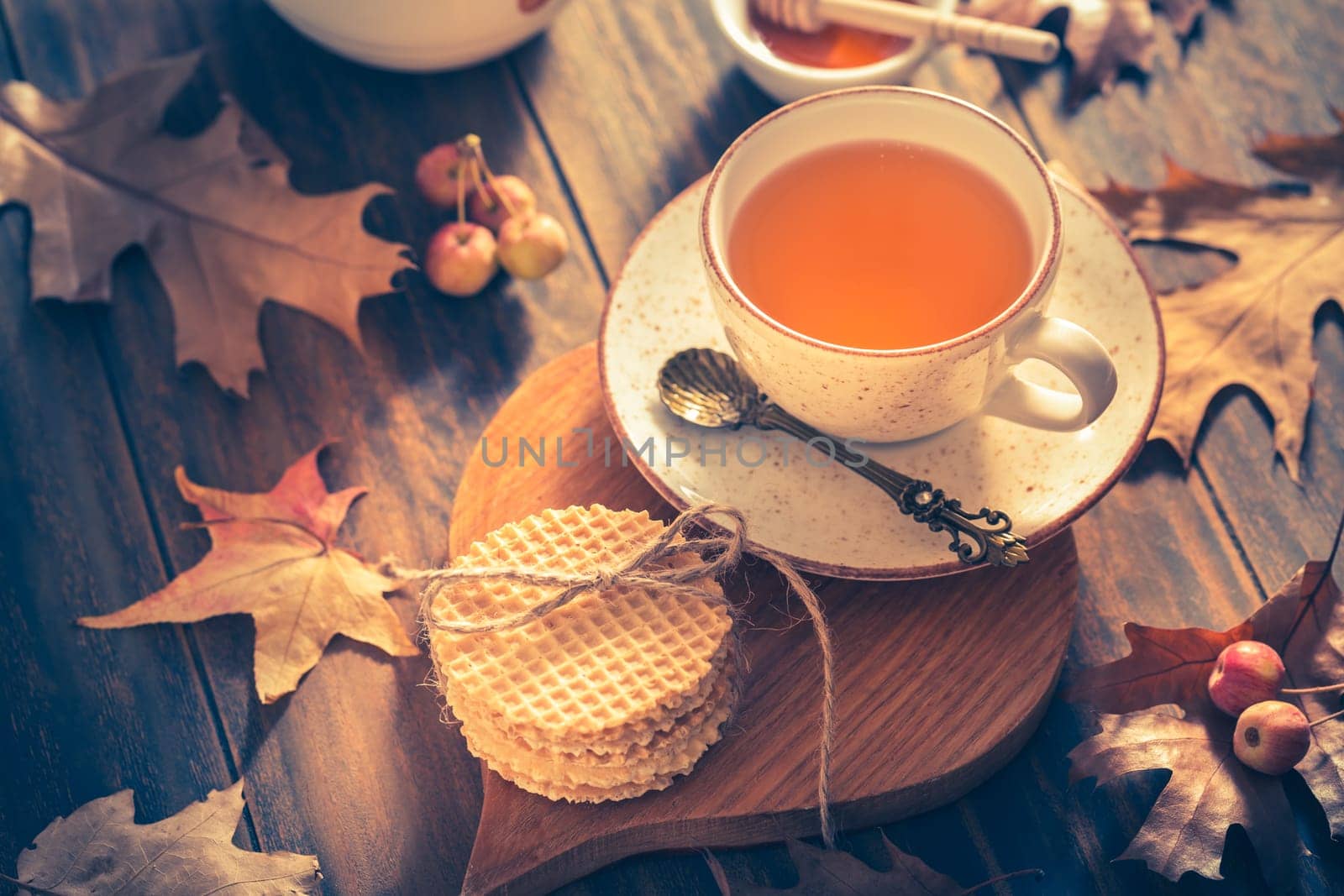 Hot tea with honey, homemade wafer biscuit and autumn leaves on wooden background