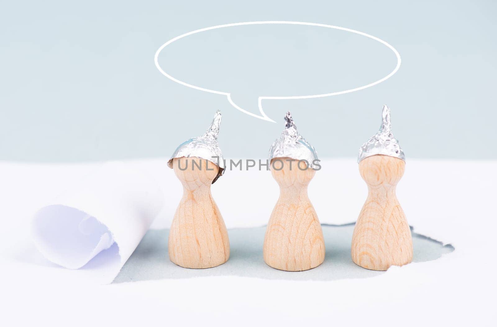 Three wooden figures wearing an alu hut, conspiracy theories, tin foil, symbolic, speech bubble, torn paper