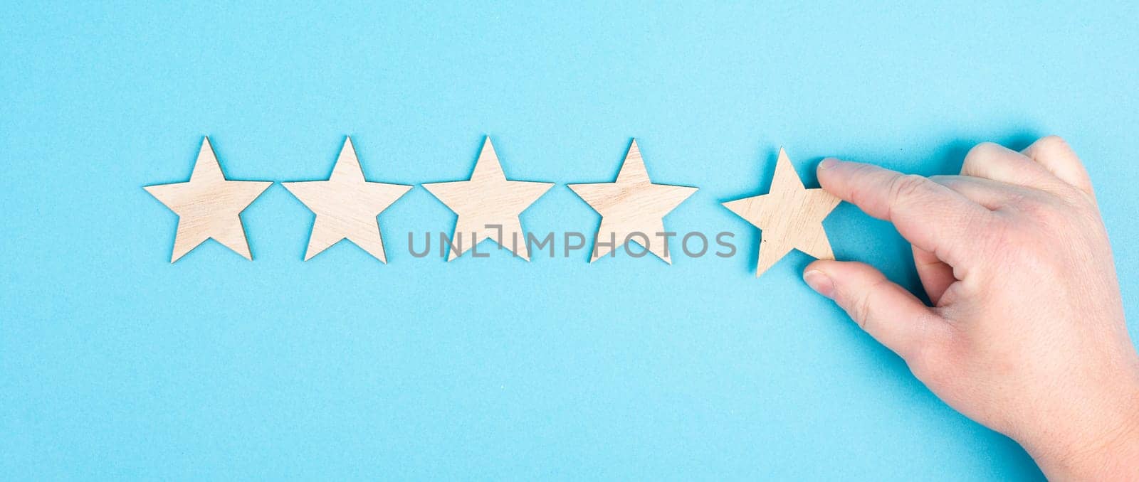 Five stars on a blue colored background, hand put the last star in the row, rating, giving feedback