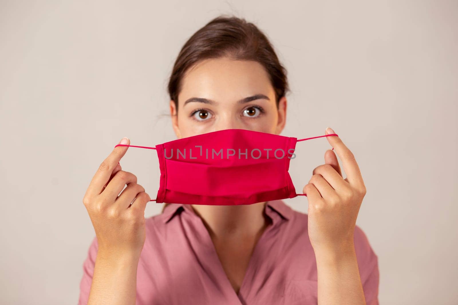 Attractive girl in pink clothing showing a protective cloth mask to the camera before putting it on. Female medical worker in studio with a flu mask in her hands.