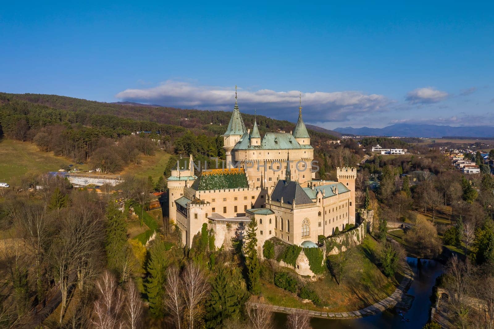 Popular tourist destination of Bojnice castle on a good weather day, with moat, greenery and forest around it. Medieval chateau from bird's eye view.