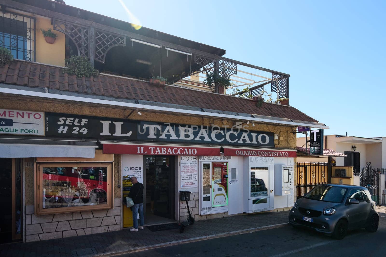 Civitavecchia. Italy - January 26, 2025: Tobacco shop in Civitavecchia, Italy, featuring a self-service kiosk and 24-hour service. The storefront includes signage and a small car parked in front.
