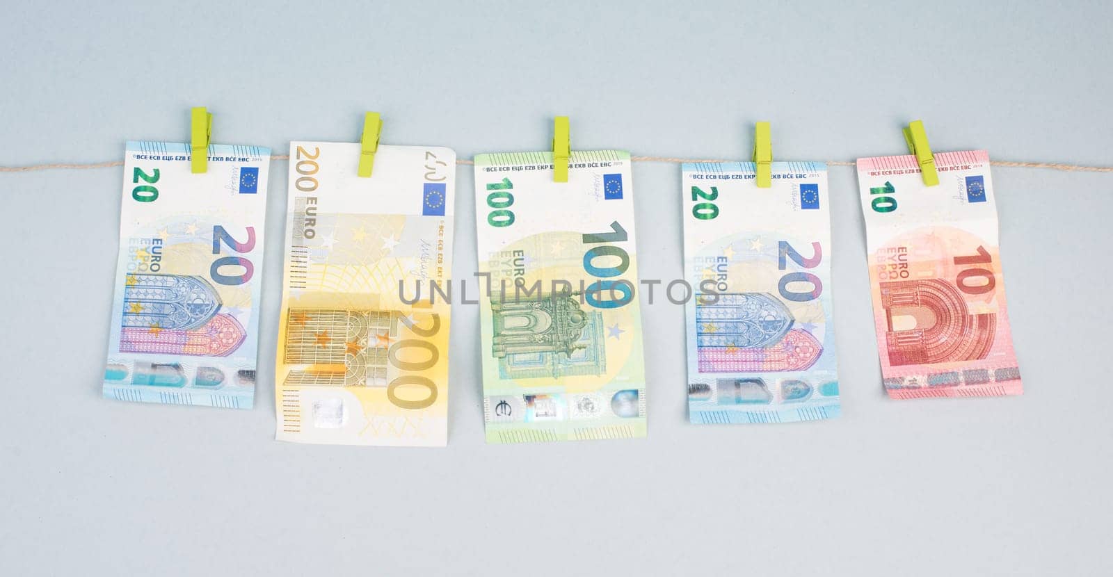 Money is hanging on a washing line, grey background, copy space, Euro banknotes, drying after laundry, european currency