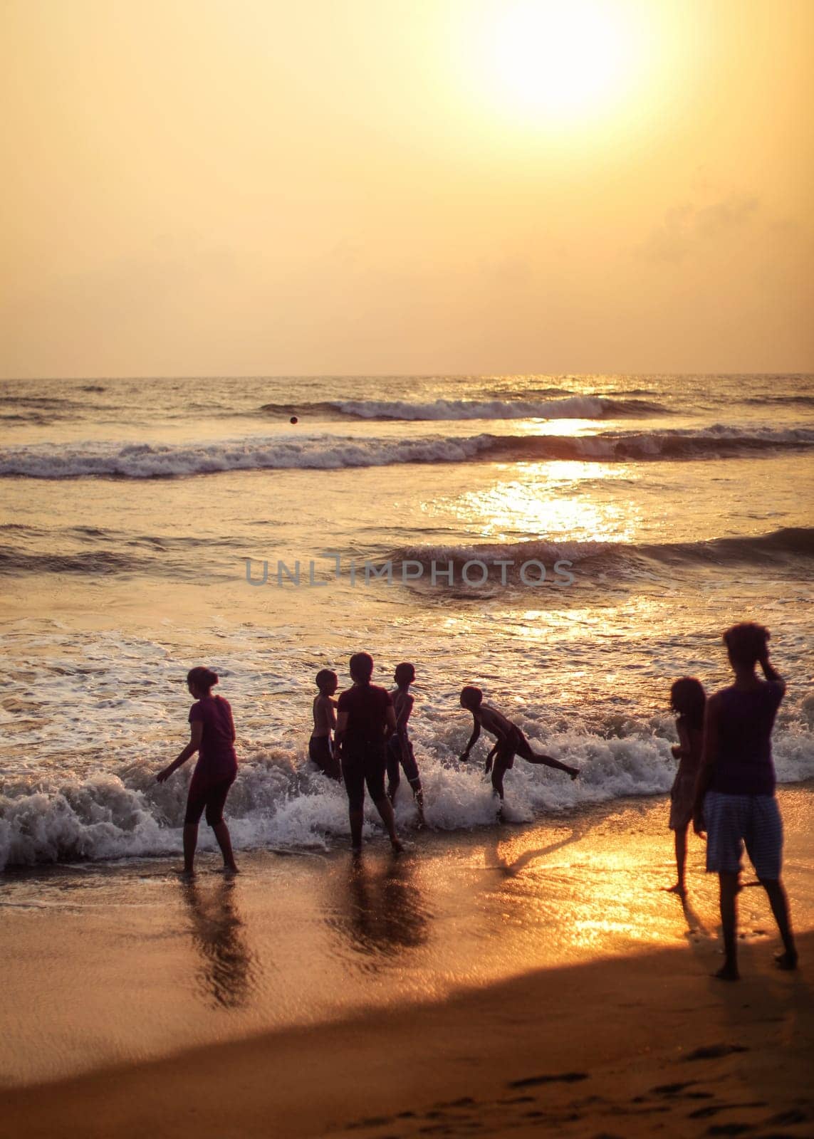 Kalutara, Sri Lanka - April 15, 2017: Silhouettes of people, mostly children playing on the beach, sea and golden sunset afternoon light in background.