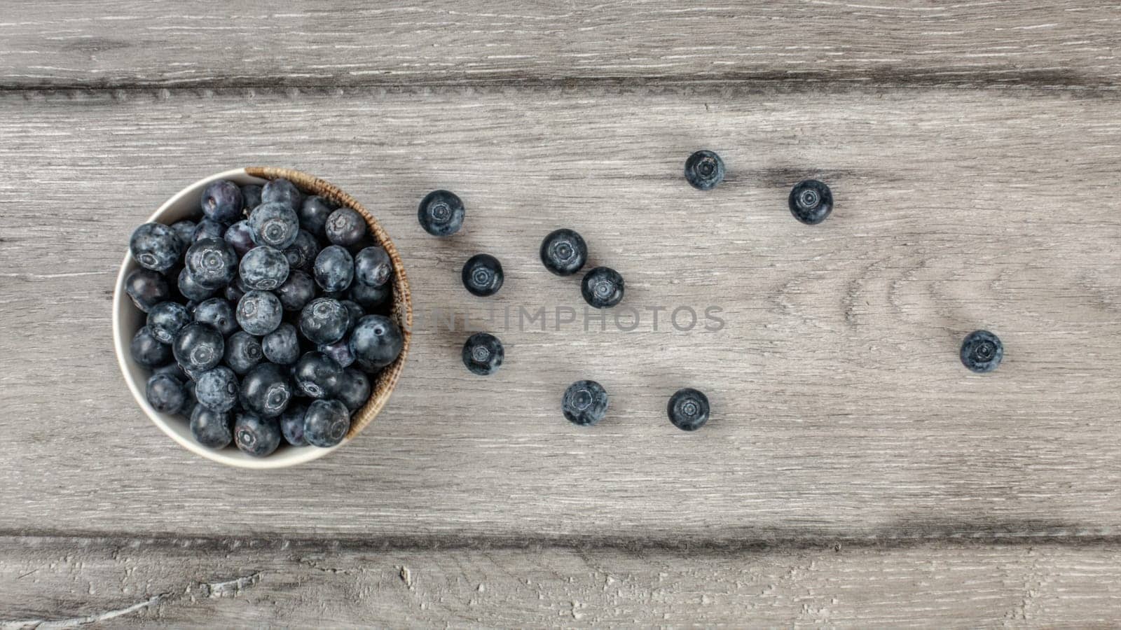 Table top view - small bowl of blueberries, some of them spilled on rustic desk.