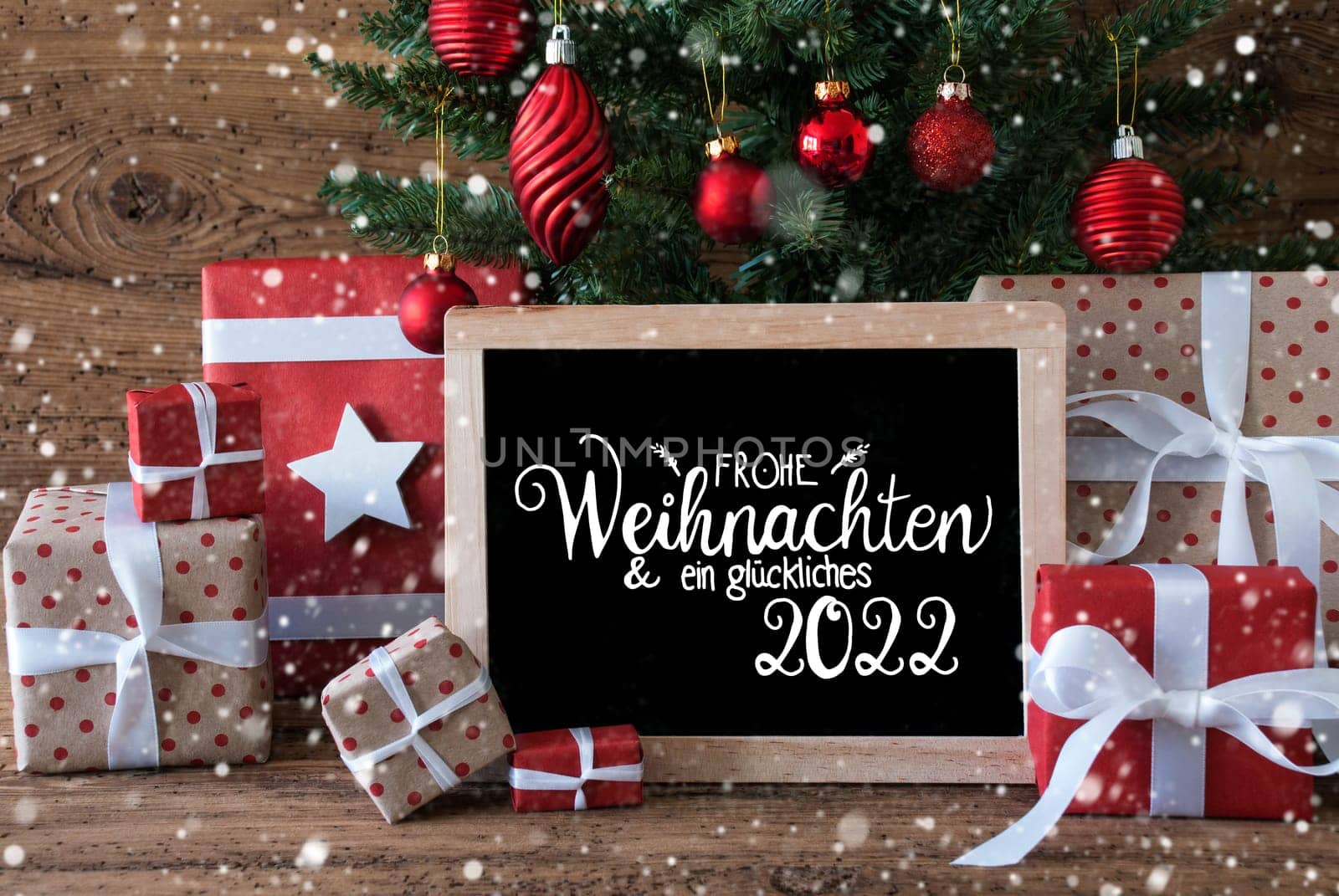 Blackboard With German Text Frohe Weihnachten Und Ein Glueckliches 2022 Means Merry Christmas And A Happy 2022. Christmas Tree With Decoration Like Balls, Gifts And Presents