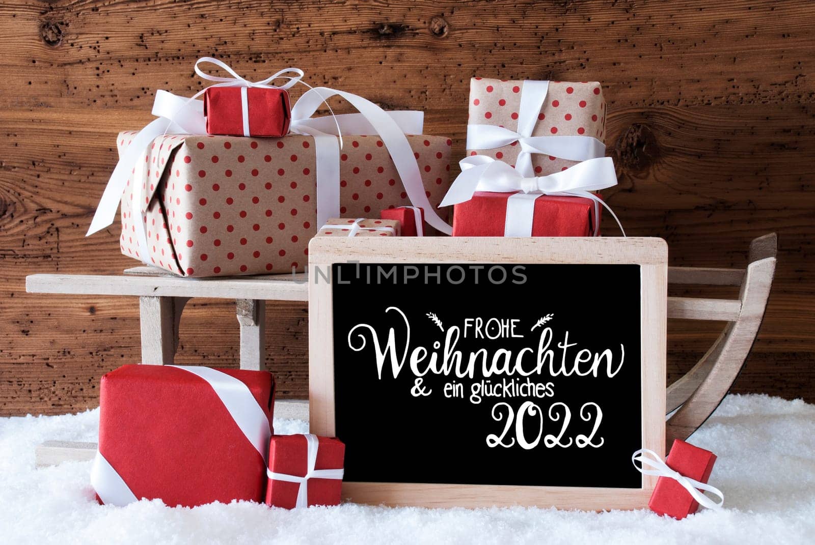 Blackboard With German Calligraphy Frohe Weihnachten Und Ein Glueckliches 2022 Means Merry Christmas And A Happy 2022. Sled With Christmas Gift And Presents. Wooden Background With Snow.