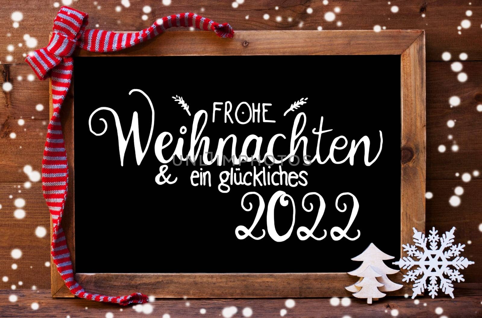 Chalkboard With German Calligraphy Frohe Weihnachten Und Ein Glueckliches 2022 Means Merry Christmas And A Happy 2022. Christmas Decoration Like Tree And Bow. Wooden Background And Snowflakes
