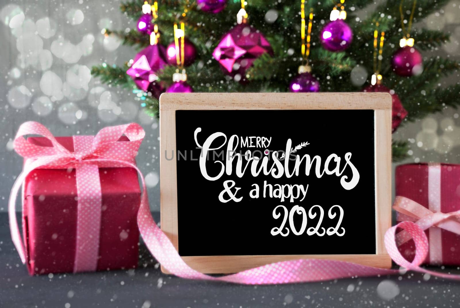 Blackboard With Egnlish Calligraphy Merry Christmas And Happy 2022. Christmas Tree With Purple Ball Ornament, Pink Gift And Bokeh Effect And Snowflakes
