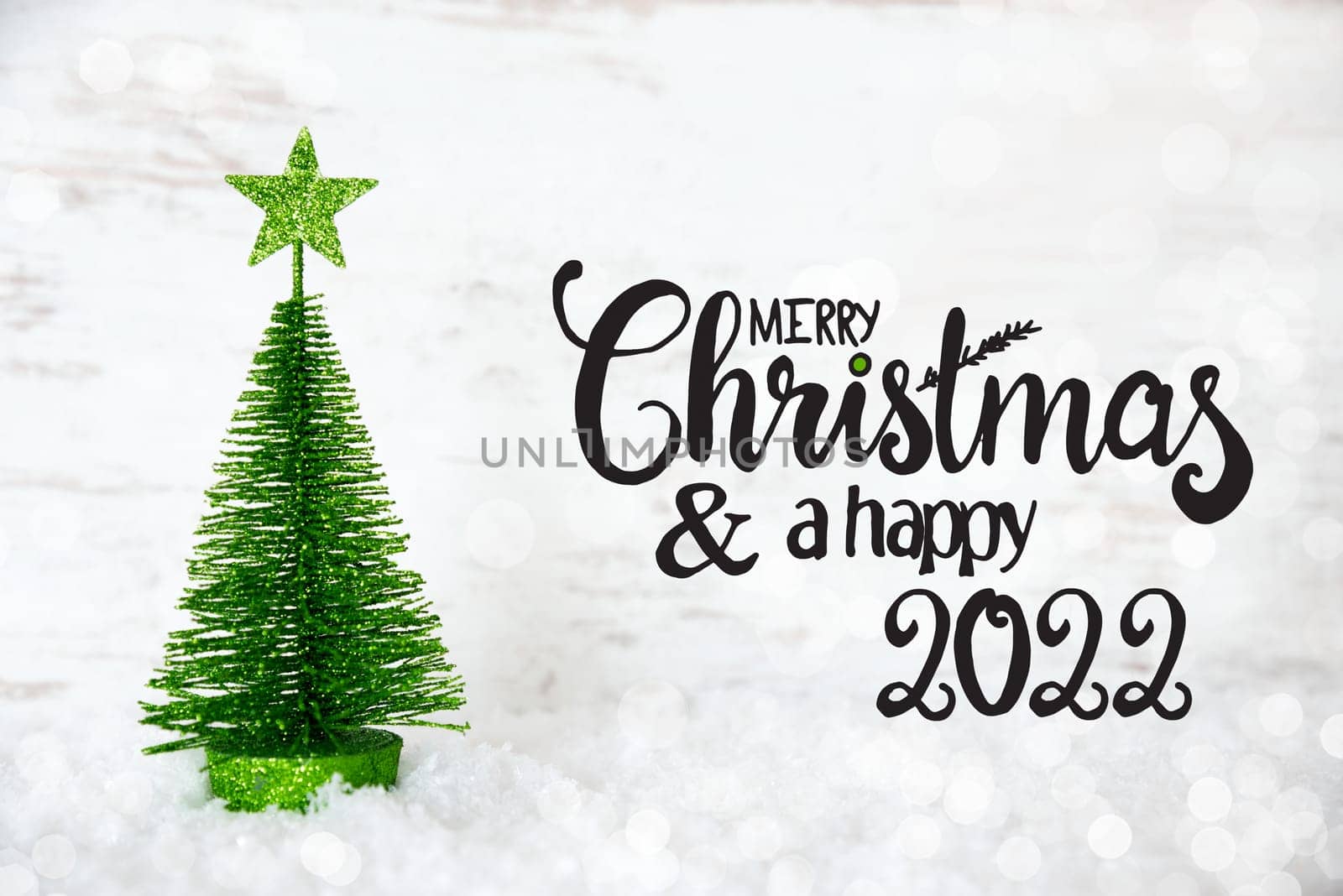 English Calligraphy Merry Christmas And A Happy 2022. One Green Christmas Tree With Star Ornament. Lights Background With Snow