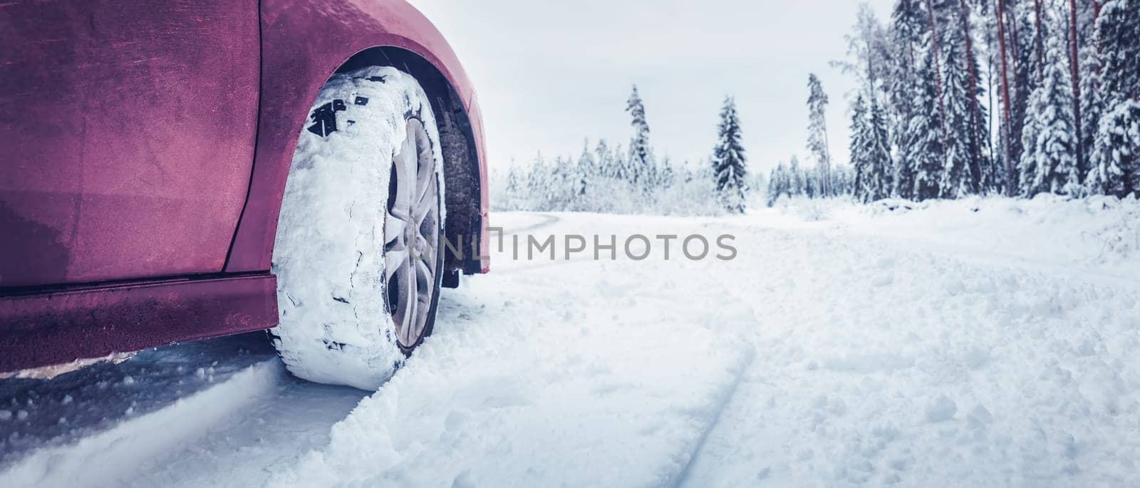 Panoramic view of the red car on the snowy road. Concept of the danger of driving on a winter road and travelling by auto in Christmas holidays.