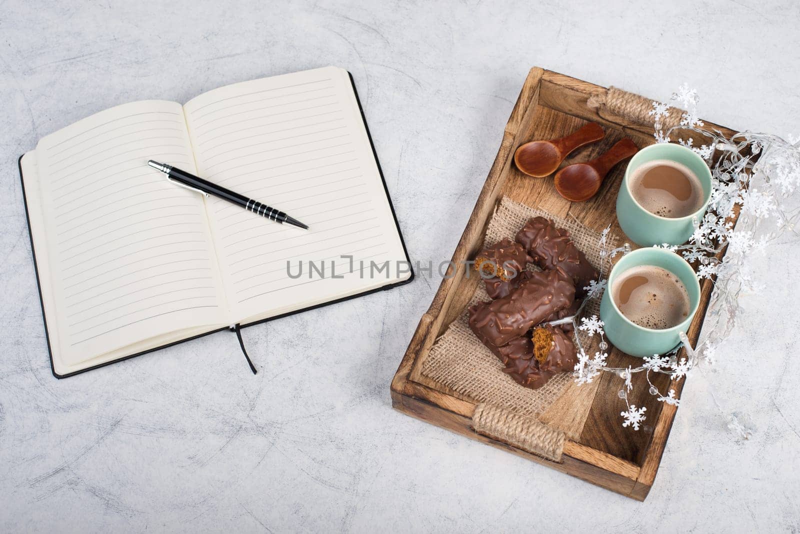 Coffee cups and chocolate coated gingerbread in a wooden basket, christmas season empty copy space, book with a pen