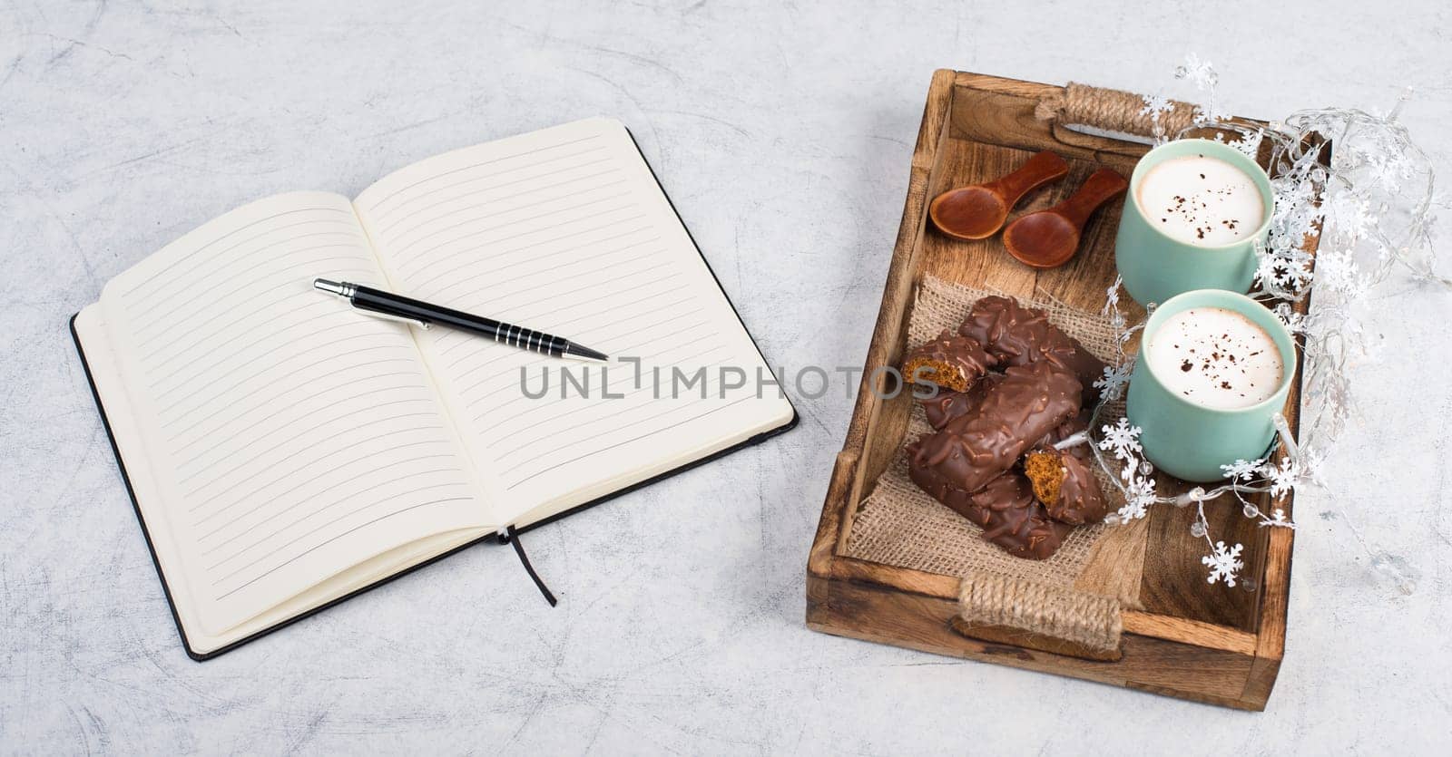 Coffee cups and chocolate coated gingerbread in a wooden basket, christmas season empty copy space, book with a pen