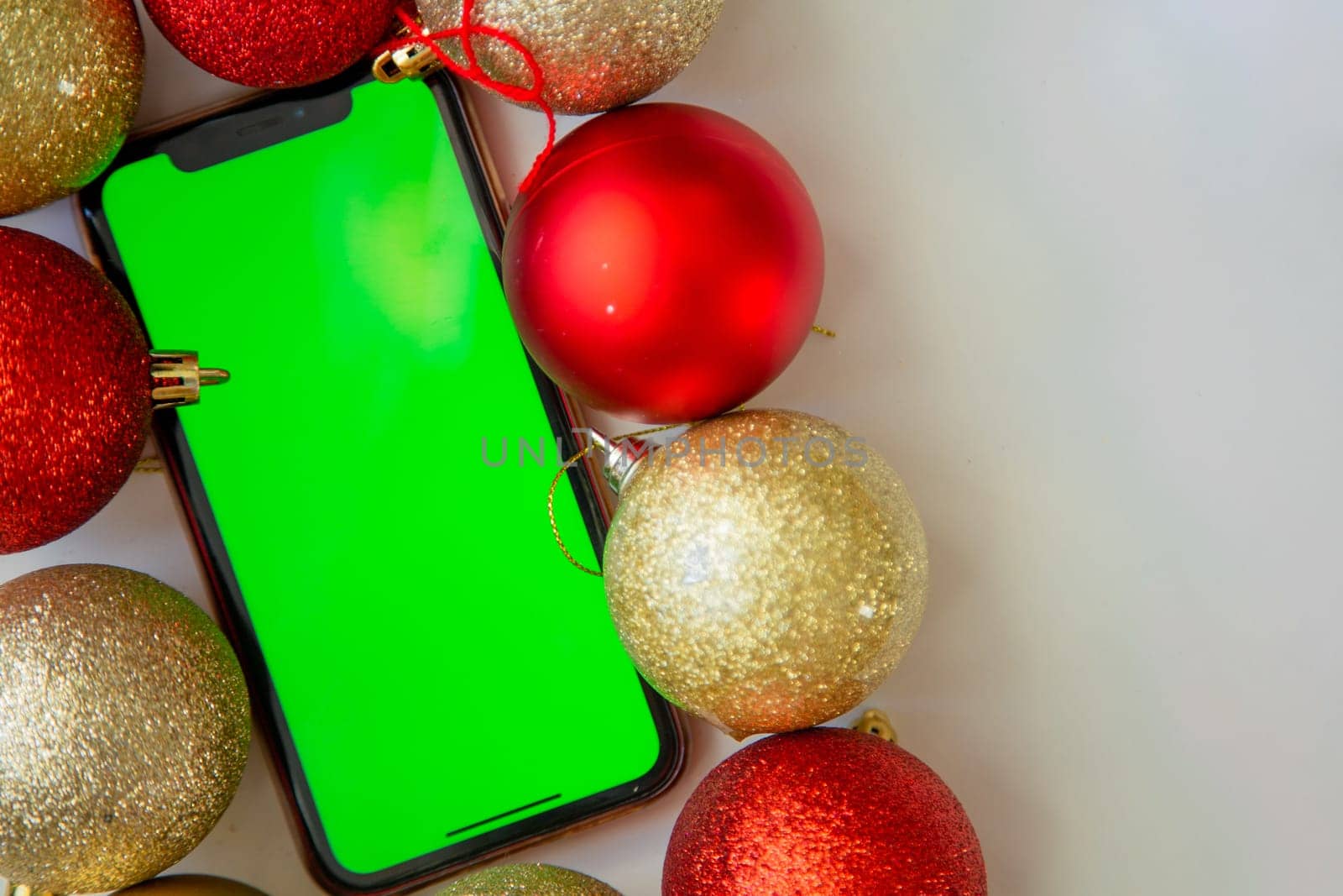 A phone with a green screen lies among the golden and red Christmas balls. High quality photo
