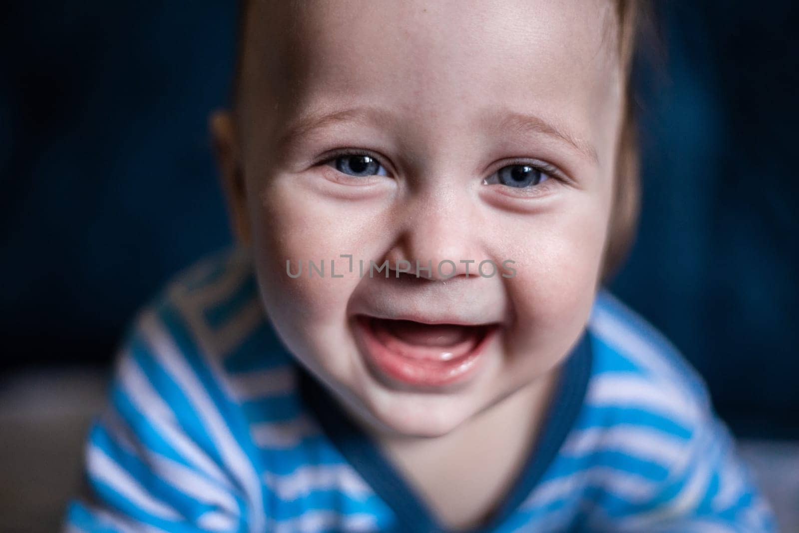 A smiling toothless kid in a striped blouse laughs, face close-up. . High quality photo