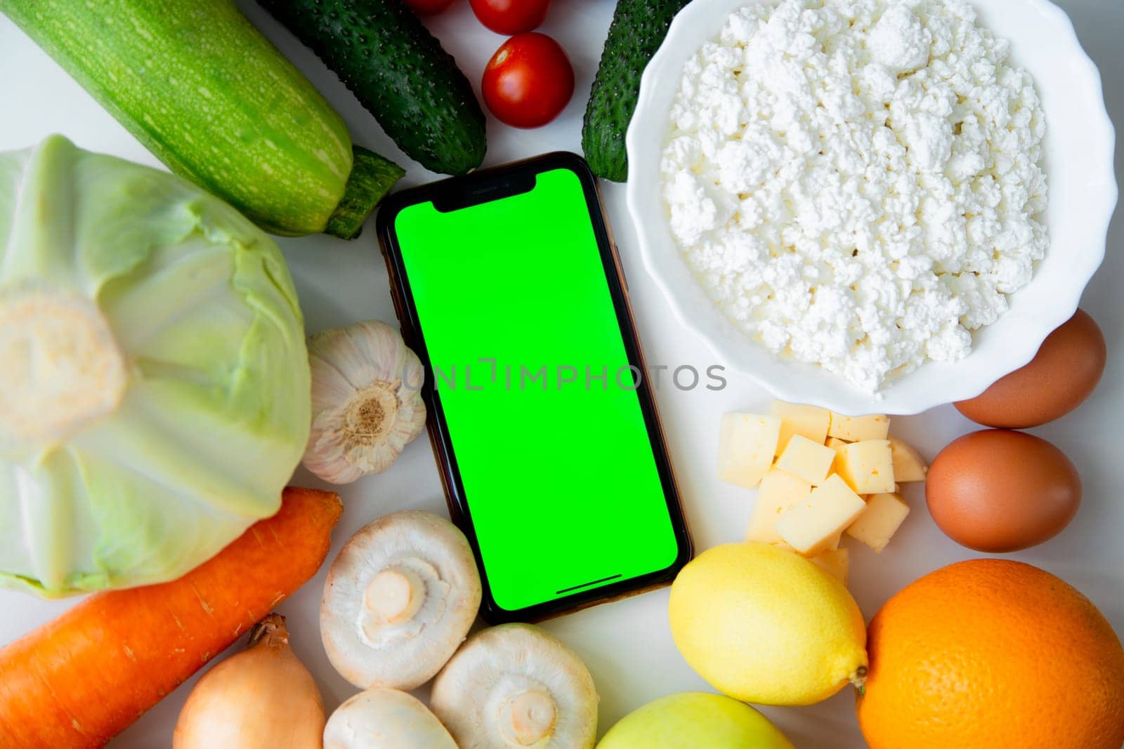 A phone with a green screen lies among fruits, vegetables and dairy products. High quality photo