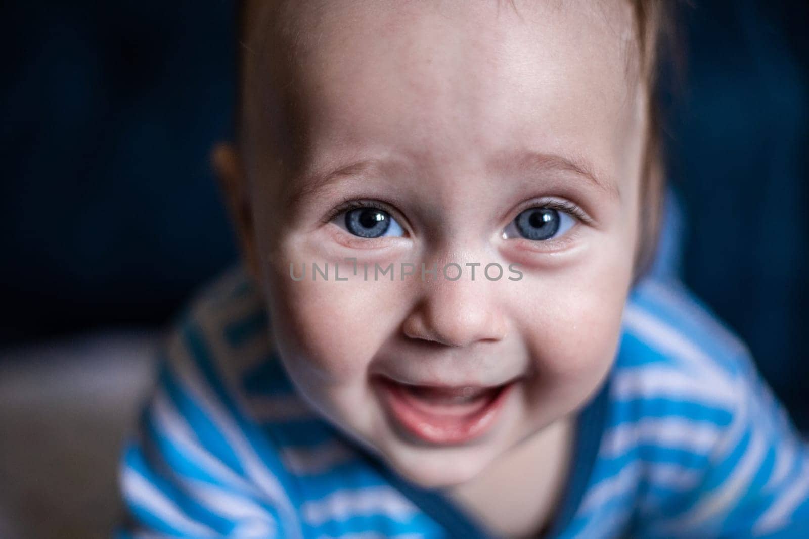 A smiling toothless kid in a striped blouse laughs, face close-up. . High quality photo
