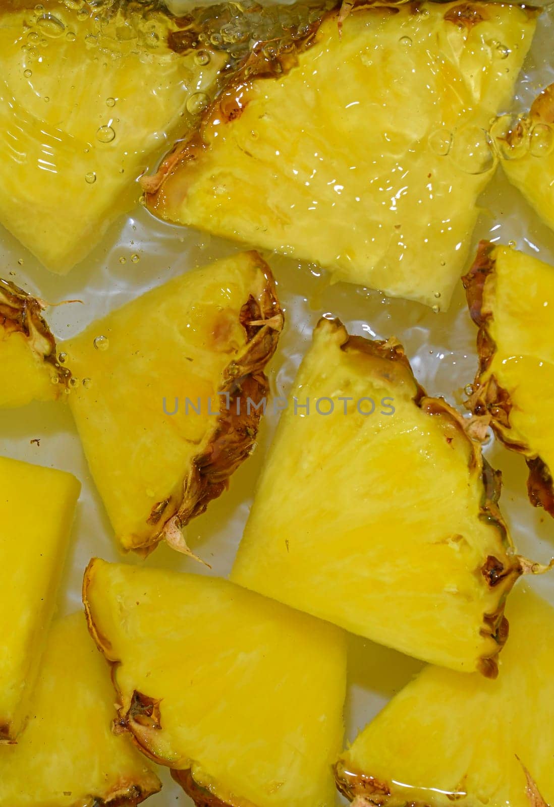 Close up view of the yellow pineapple slices in lemonade background. Texture of cooling sweet summer's drink with macro bubbles on the white background. Flat design. Vertical image.