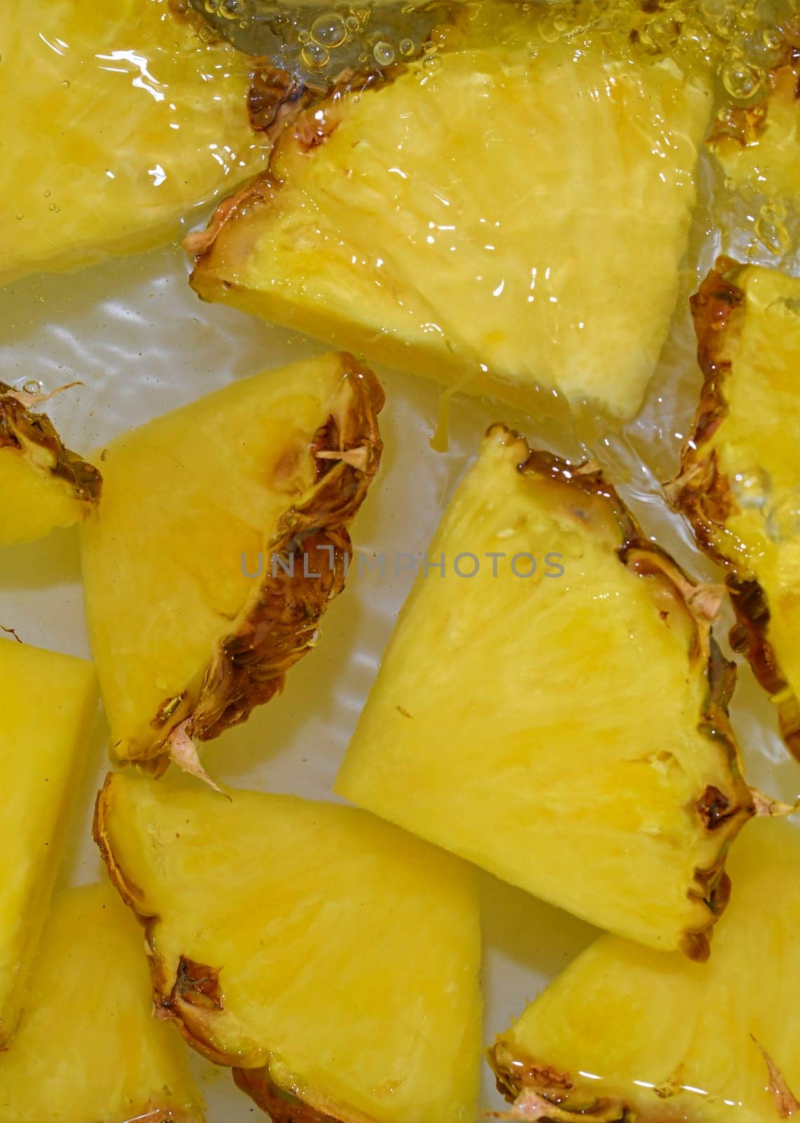 Close up view of the yellow pineapple slices in lemonade background. Texture of cooling sweet summer's drink with macro bubbles on the white background. Flat design. Vertical image.