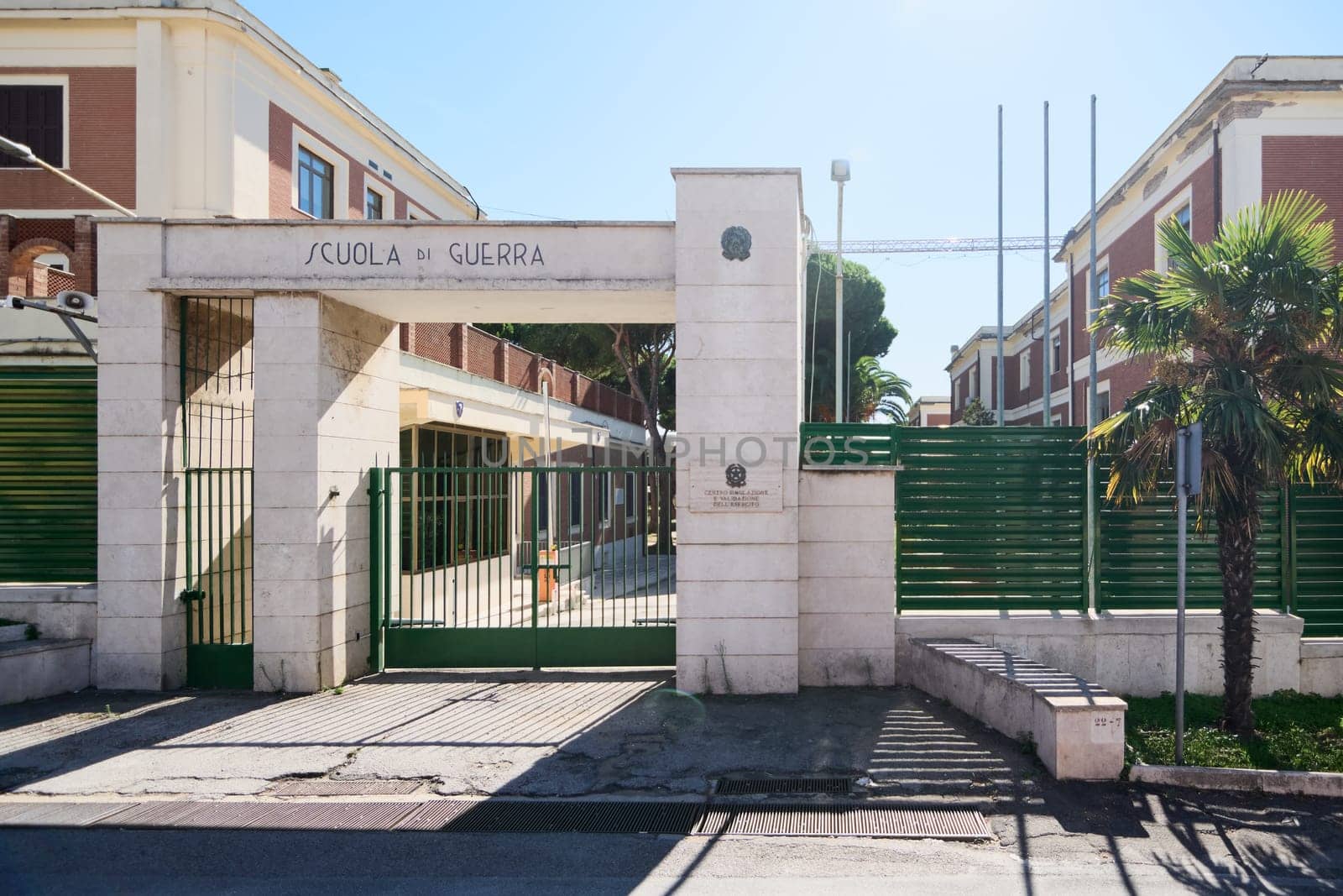 Civitavecchia. Italy - January 26, 2025: The main entrance of the Italian War School in Civitavecchia, featuring a gated entrance with a sign reading Scuola di Guerra and a red brick building in the background.