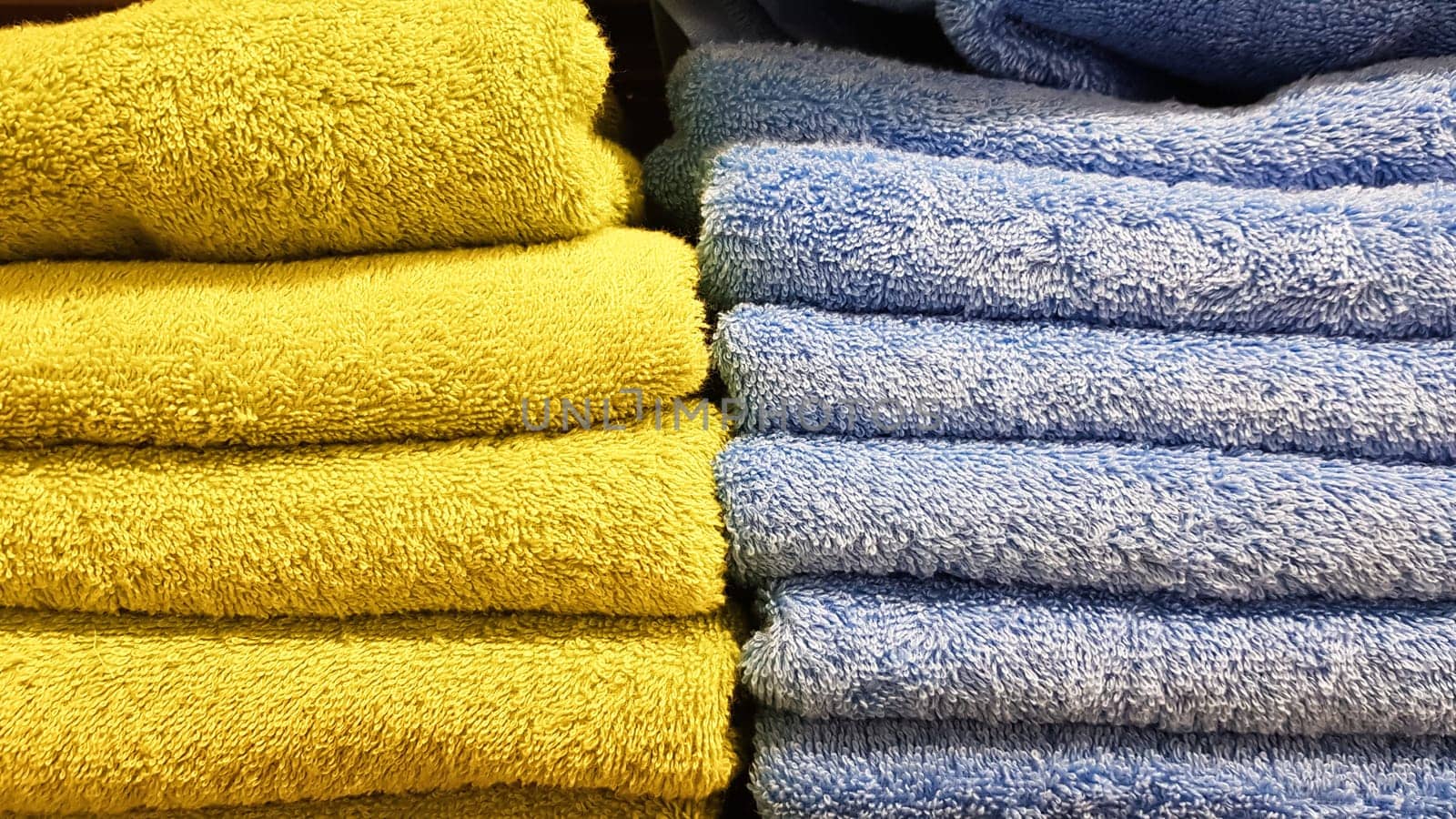 Stacks of fluffy bath towels of various colors in a store window. Terry cotton towels in a stack on the shelves of a supermarket