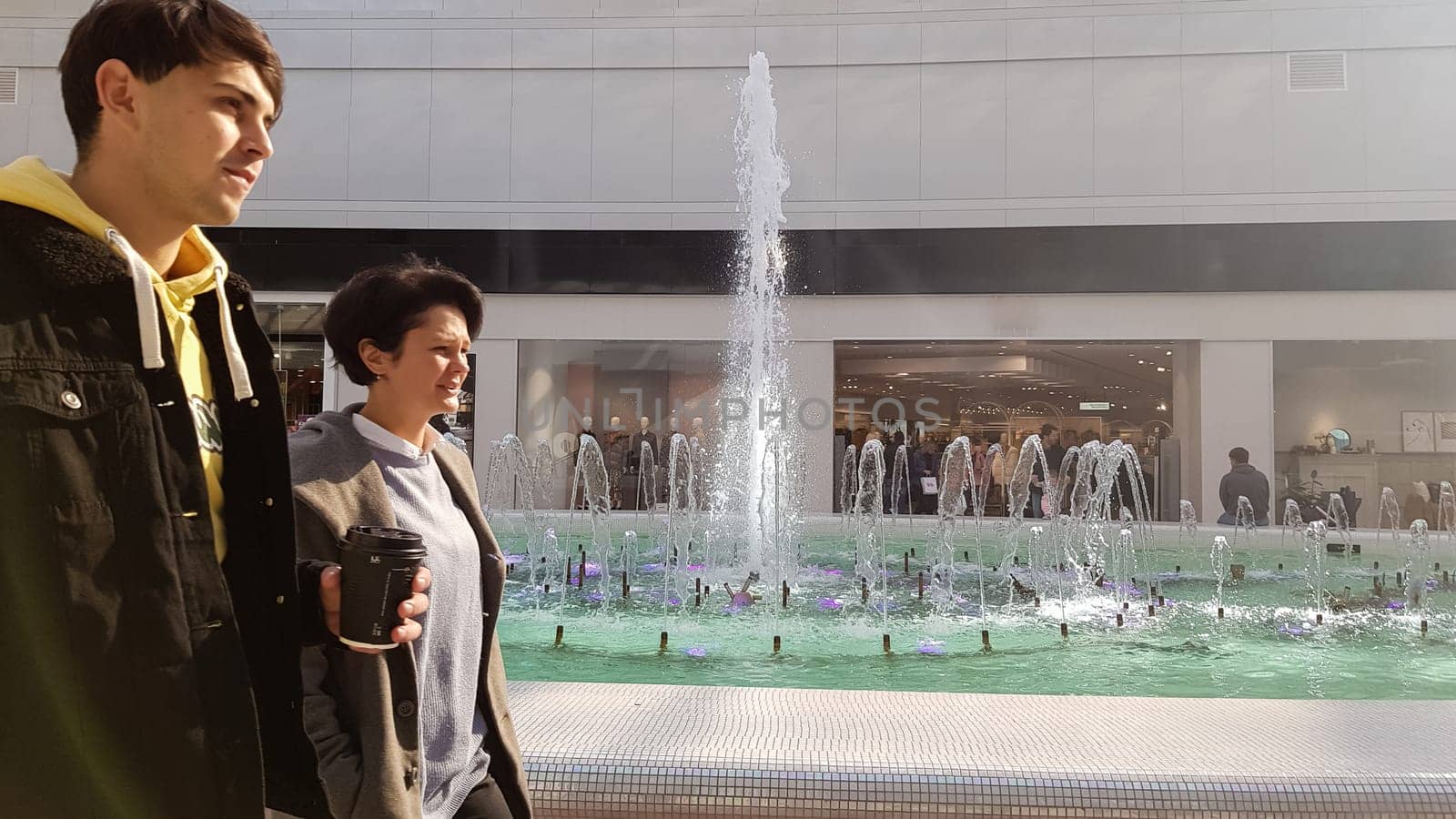 Ukraine, Kiev - February 25, 2020: a beautiful couple walking along the alley with coffee in hand. Successful couple spending time together after shopping at the mall, free space.