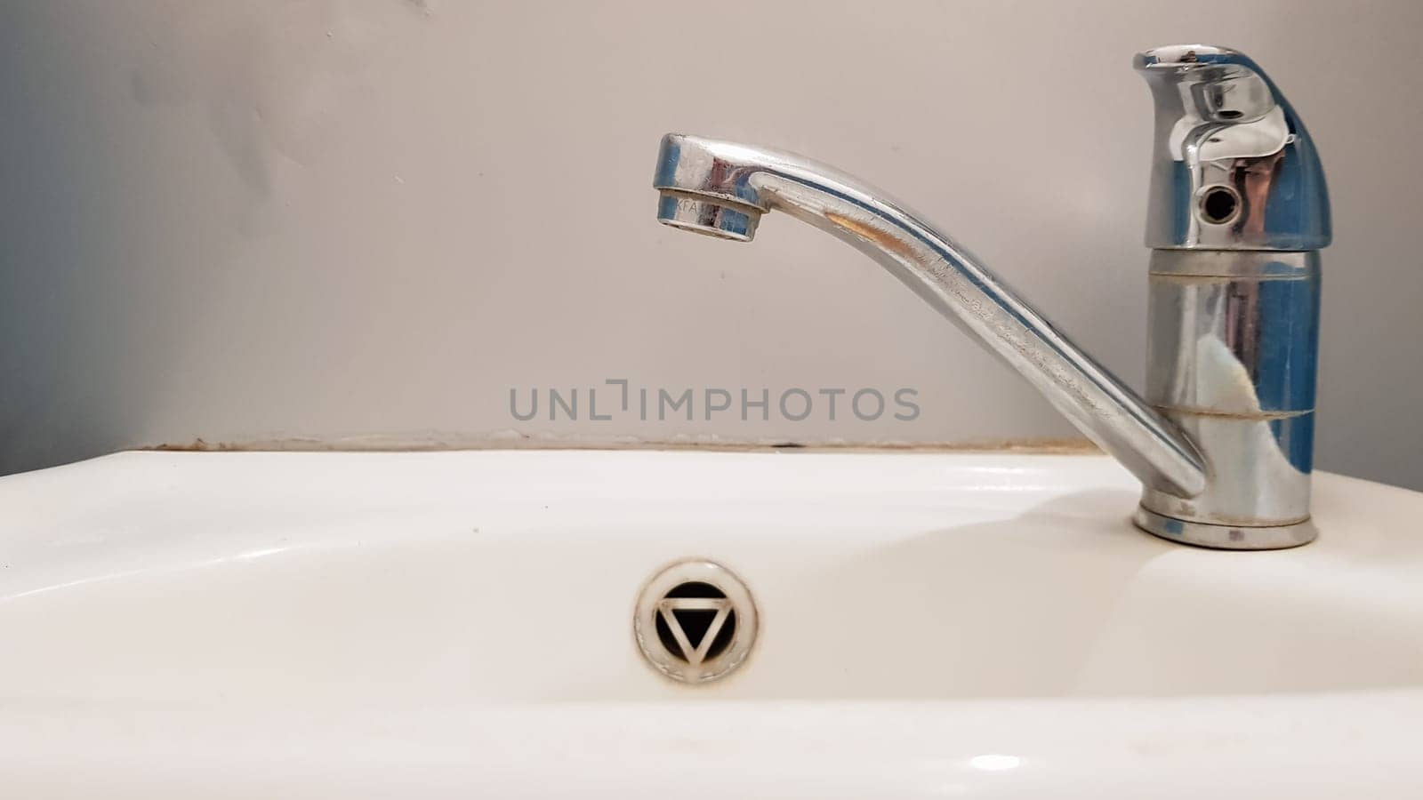 Old and dirty faucet and white ceramic washbasin sink, concept of cleaning, repairing or replacing a bathroom, toilet