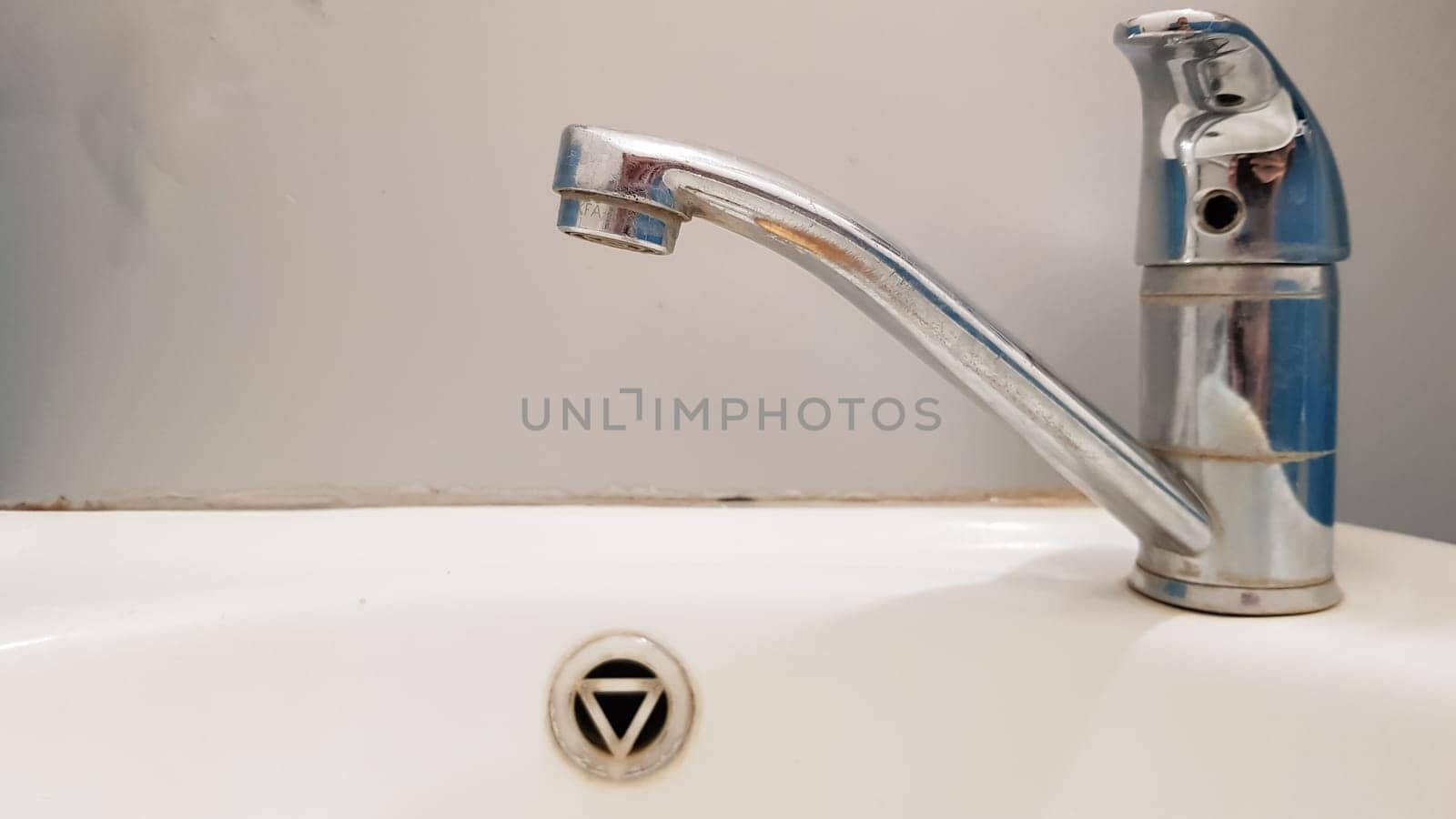 Old and dirty faucet and white ceramic washbasin sink, concept of cleaning, repairing or replacing a bathroom, toilet