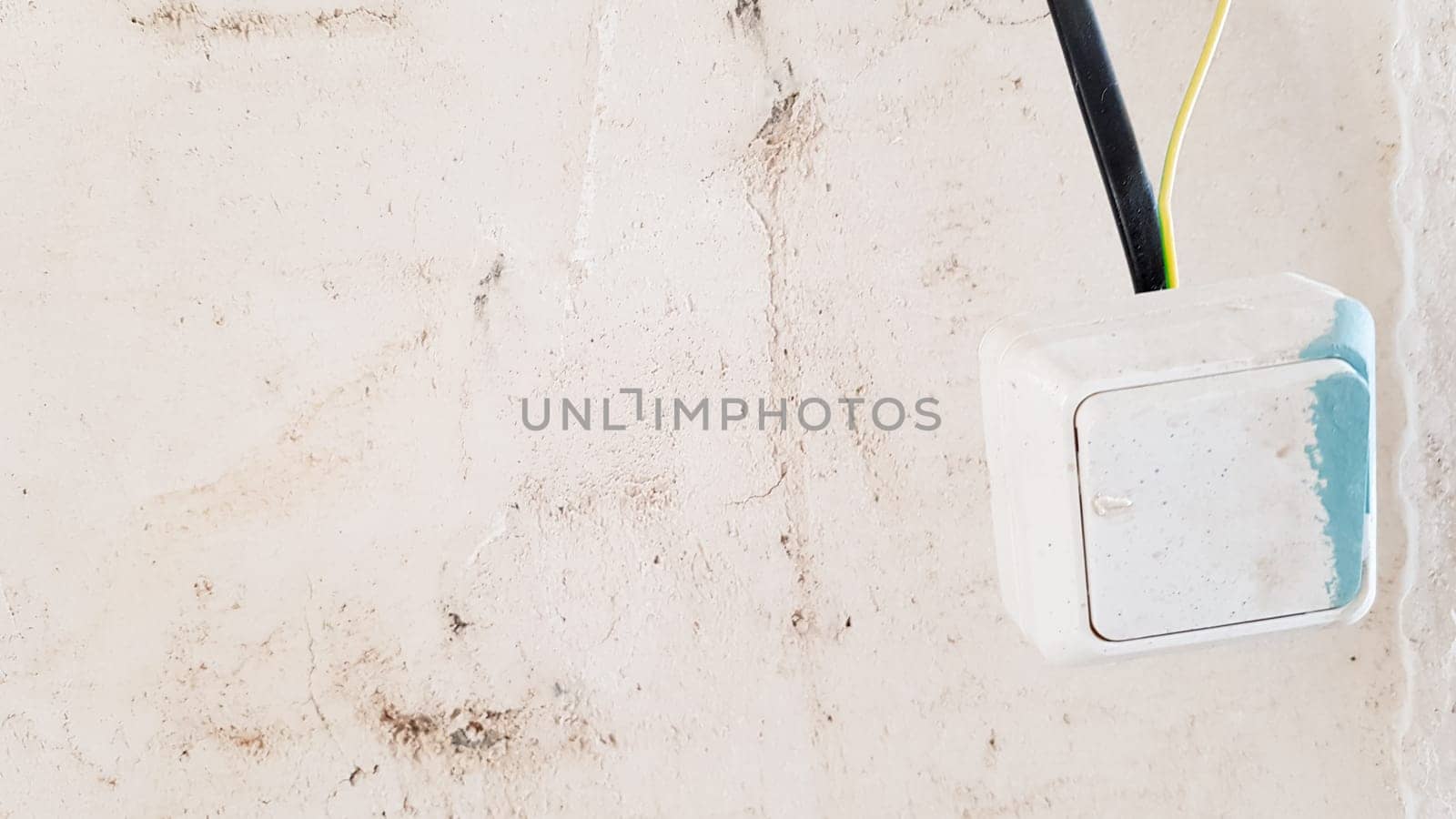 one white light switch in paint and putty is temporarily hanging on a black wire during repair against the background of an unfinished wall. open the wires
