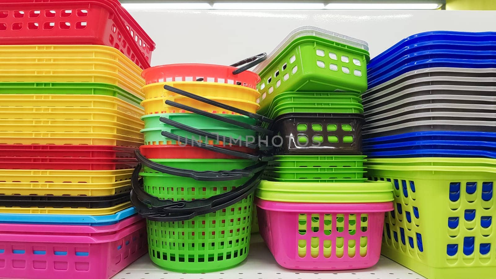 Multi-colored plastic containers of different shapes and sizes with and without lids, stacked in a pile on a store window. Sale of boxes for storage and cleaning. Modern kitchen utensils.