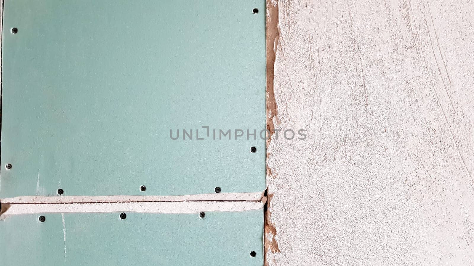 Unfinished wall in a building under construction made of plasterboard. Part of the wall is sheathed with drywall. Drywall is bolted to the wall in anticipation of plaster