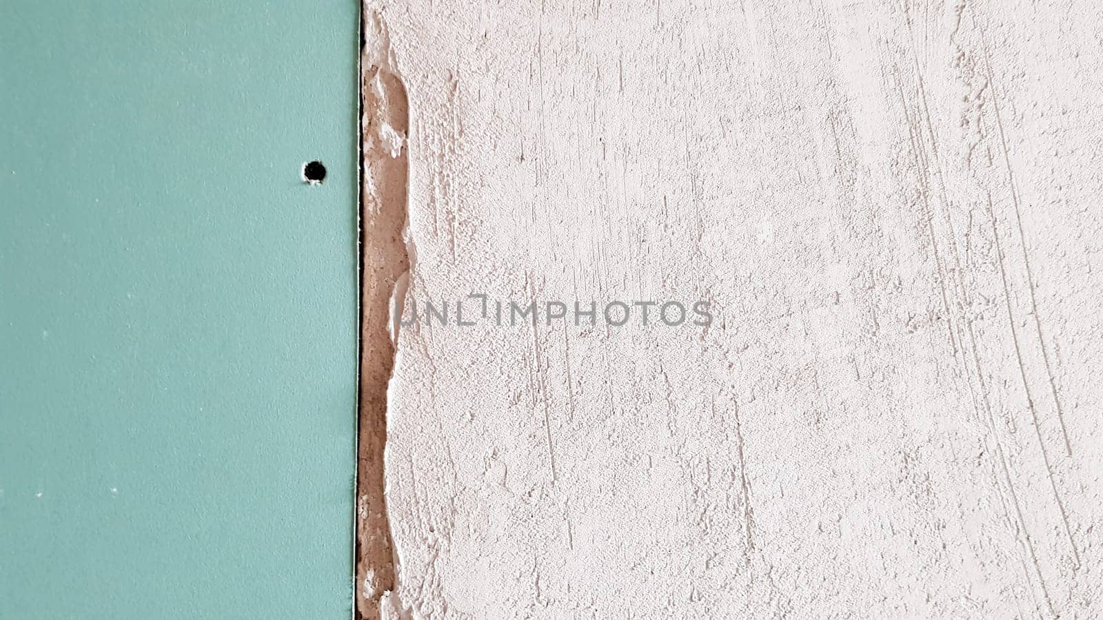 Unfinished wall in a building under construction made of plasterboard. Part of the wall is sheathed with drywall. Drywall is bolted to the wall in anticipation of plaster