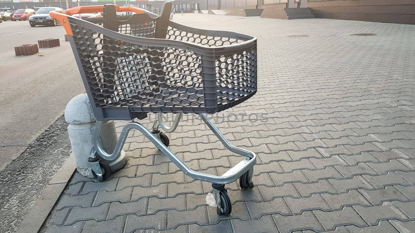 Empty grocery cart outdoor near the supermarket. Loneliness, cart isolation, quarantine, coronavirus. one empty plastic basket on wheels with yellow plastic parts left on the sidewalk near the store