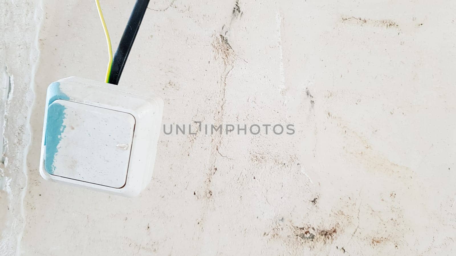 one white light switch in paint and putty is temporarily hanging on a black wire during repair against the background of an unfinished wall. open the wires