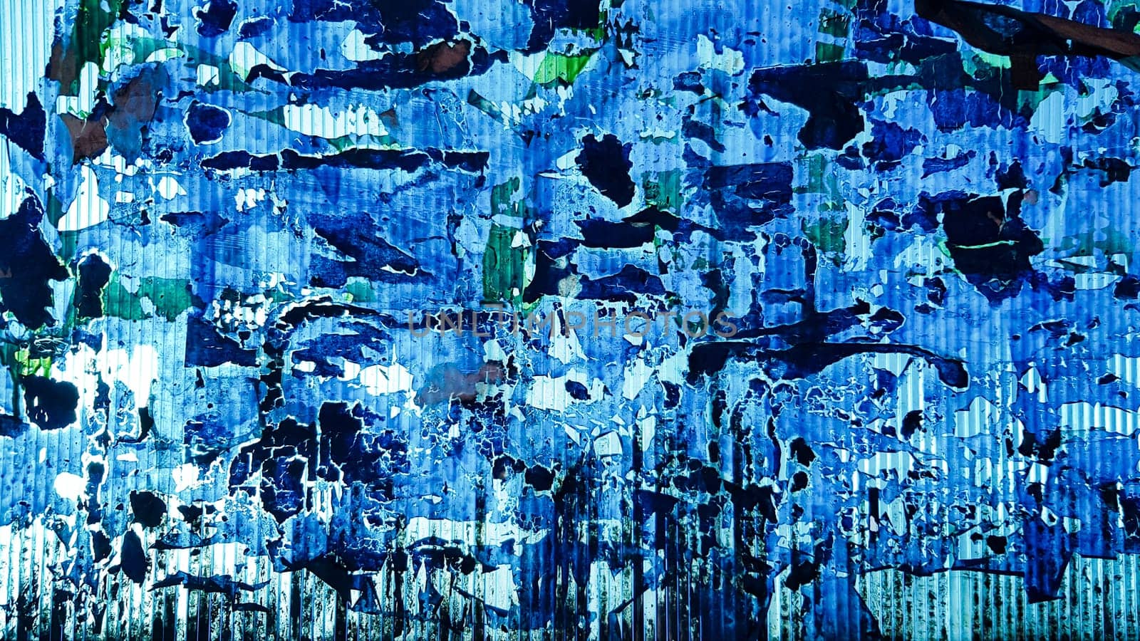 Uneven wavy plastic surface with the remains of flaky film and paper. Abstract obsolete blue background. Copy space, design. Grain blue paint wall background or texture.