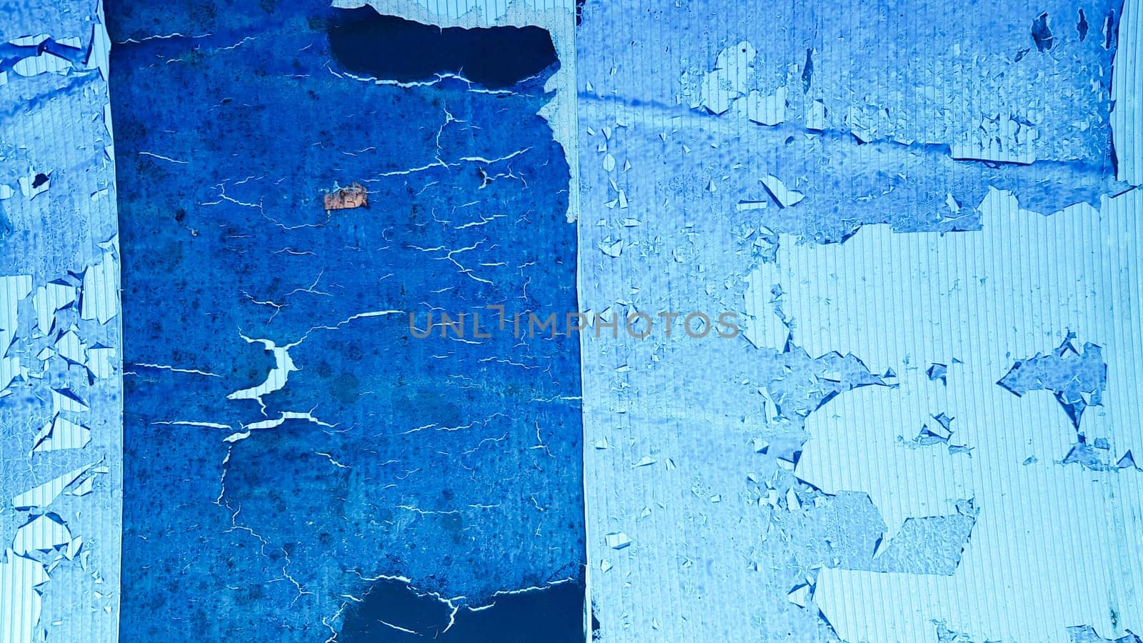 Uneven wavy plastic surface with the remains of flaky film and paper. Abstract obsolete blue background. Copy space, design. Grain blue paint wall background or texture.