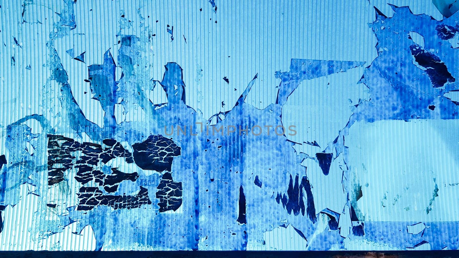 Uneven wavy plastic surface with the remains of flaky film and paper. Abstract obsolete blue background. Copy space, design. Grain blue paint wall background or texture.