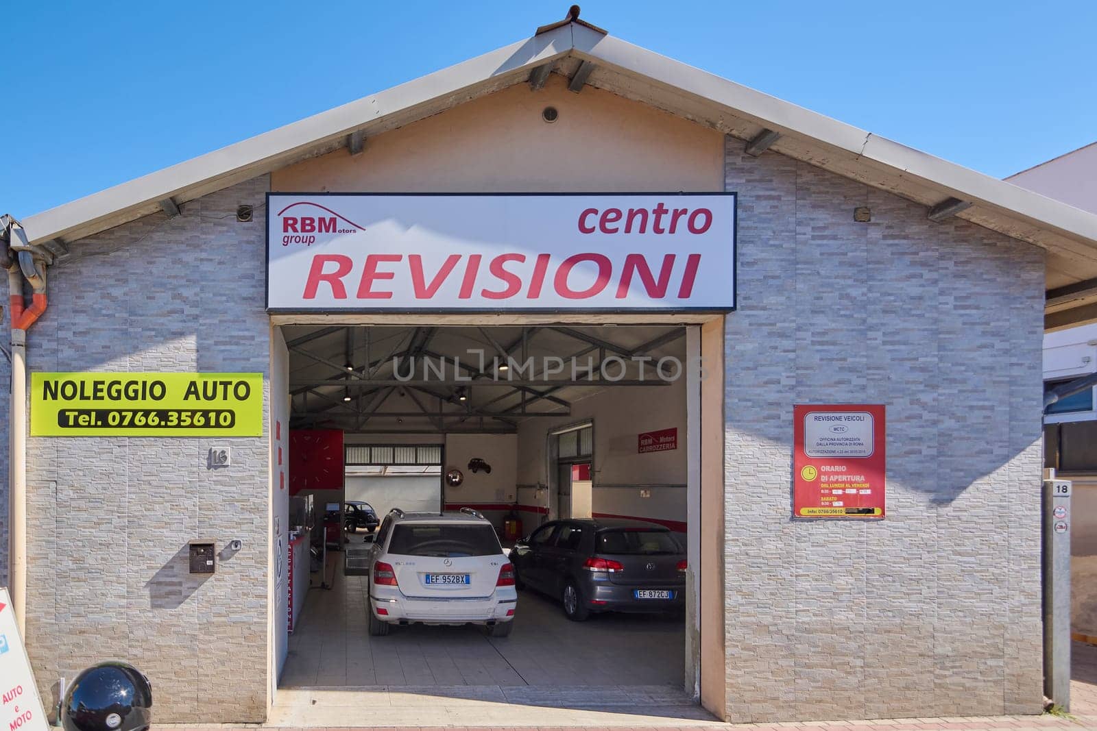 Civitavecchia. Italy - January 26, 2025: Automotive service center exterior with visible centro REVISIONI, RBM group, and NOLEGGIO AUTO signage. Two cars inside the garage.
