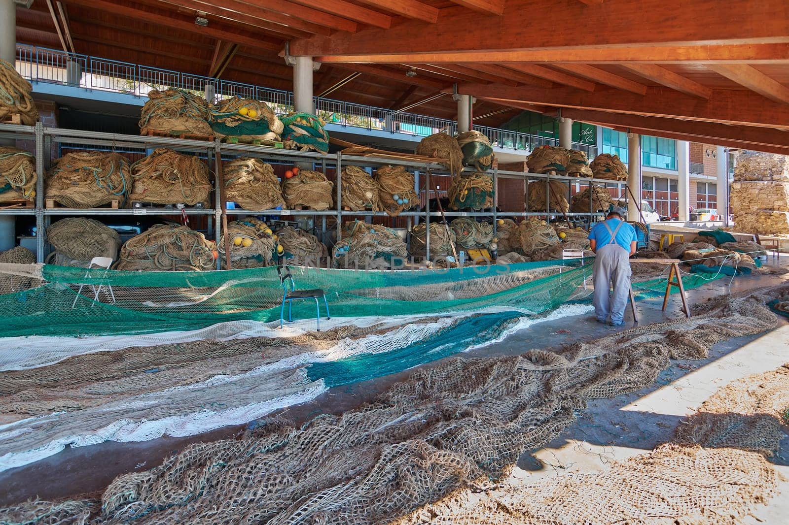 Civitavecchia, Italy - January 31, 2025: Fisherman repairing nets in a storage area in Civitavecchia, Italy. The image shows the organization and intricate work involved in maintaining the nets.