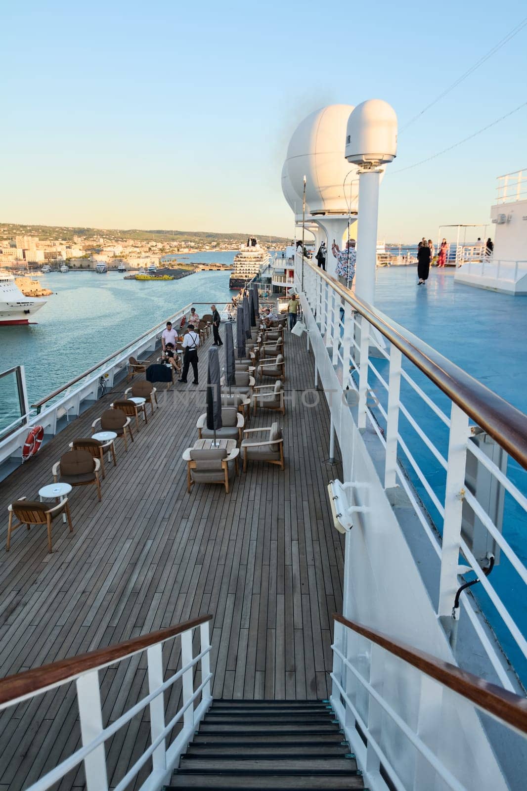 Civitavecchia, Italy - February 6, 2025: A scene of passengers on the deck of a cruise ship with wooden floors and comfortable seating, in a relaxed maritime atmosphere.