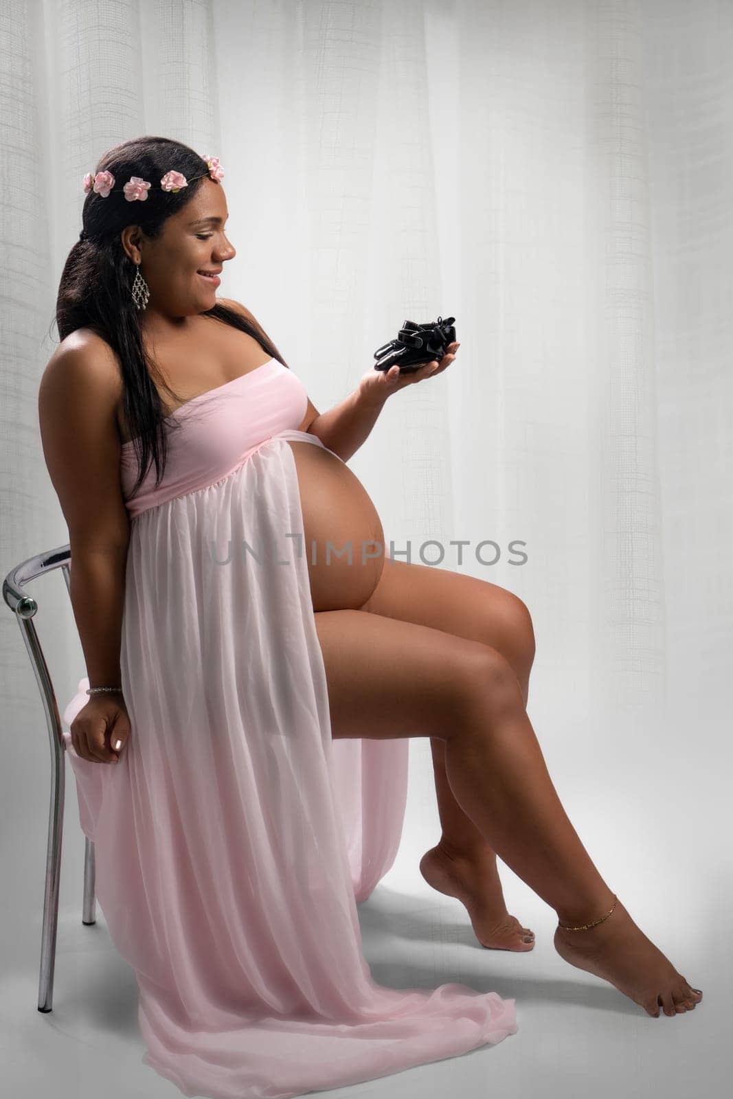 Studio photo of a happy Afro-American woman looking at some baby shoes. The woman is pregnant and her belly is visible