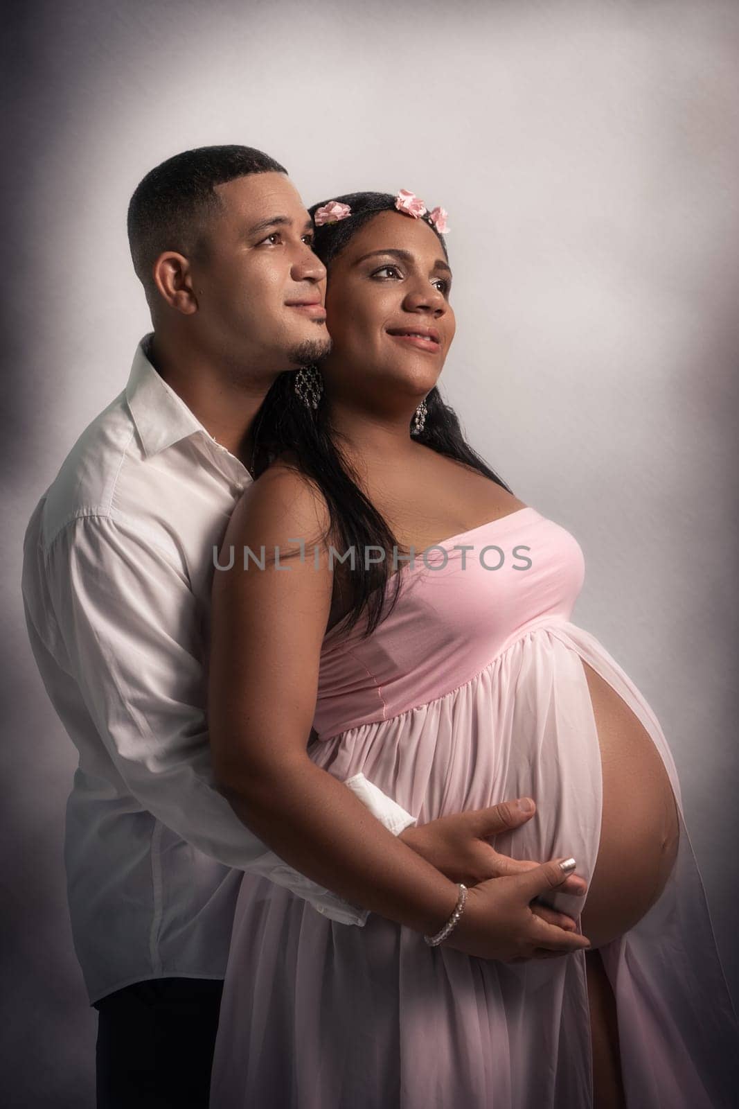 Studio shot of a young African American couple. The woman is pregnant and her belly is visible. They are both stroking the woman's belly and with a happy expression on their faces.