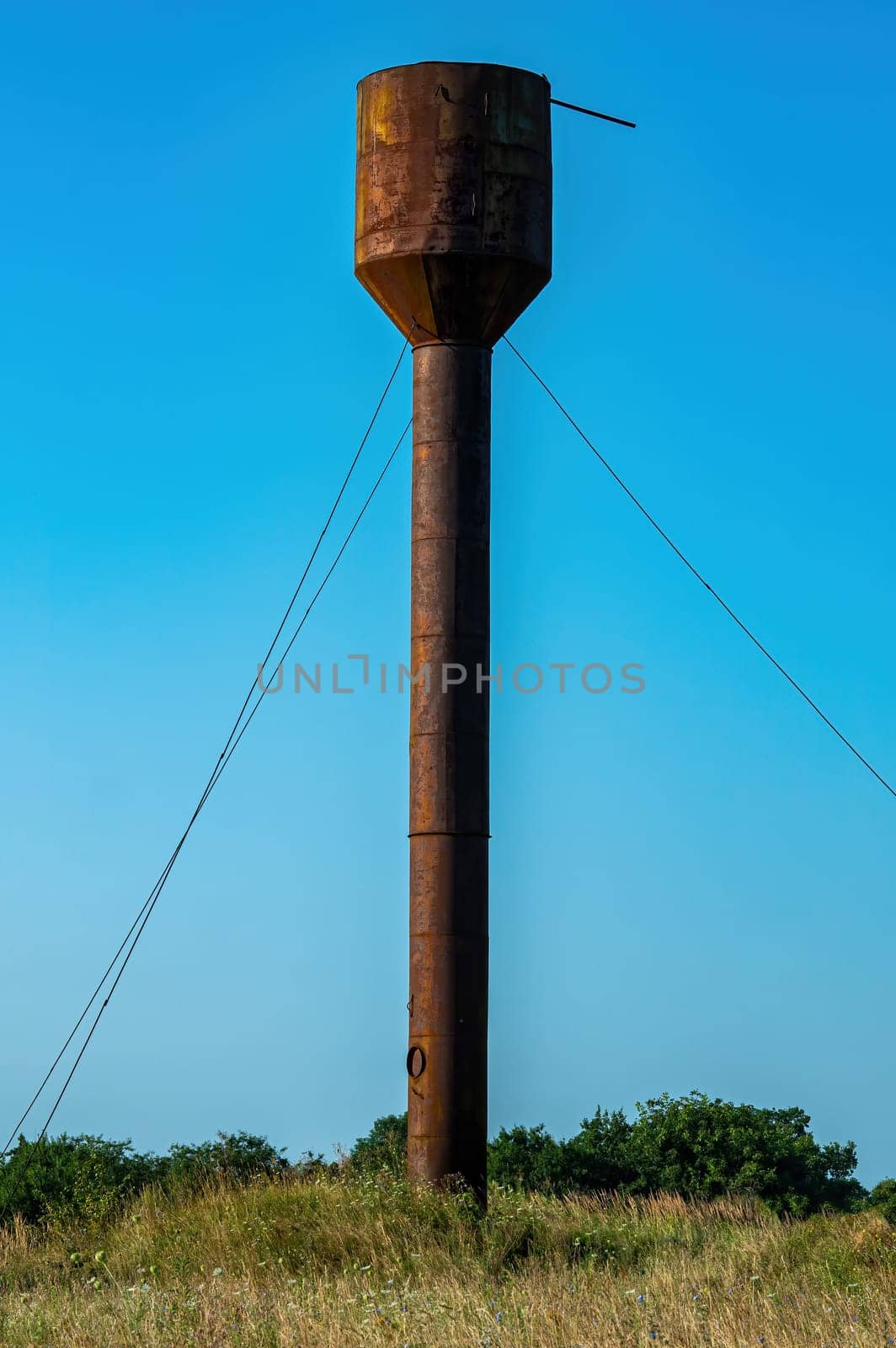 Old rusty water tower in the field against the blue sky. Water tower. Industrial equipment. Metal construction. Blue sky. Sunny day. High. Countryside. Background image.