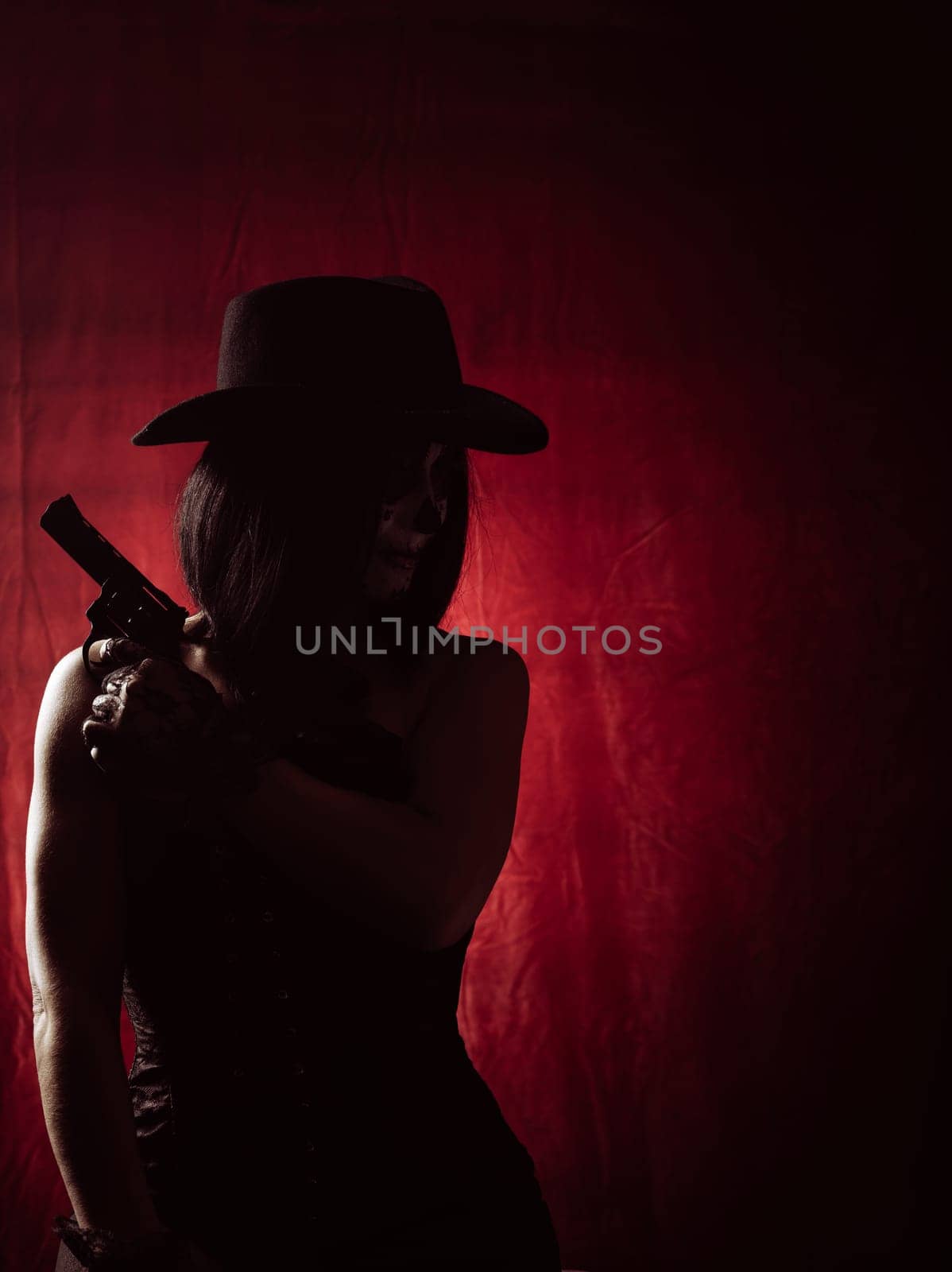 woman in corset and black hat holding revolver on red background, silhouette