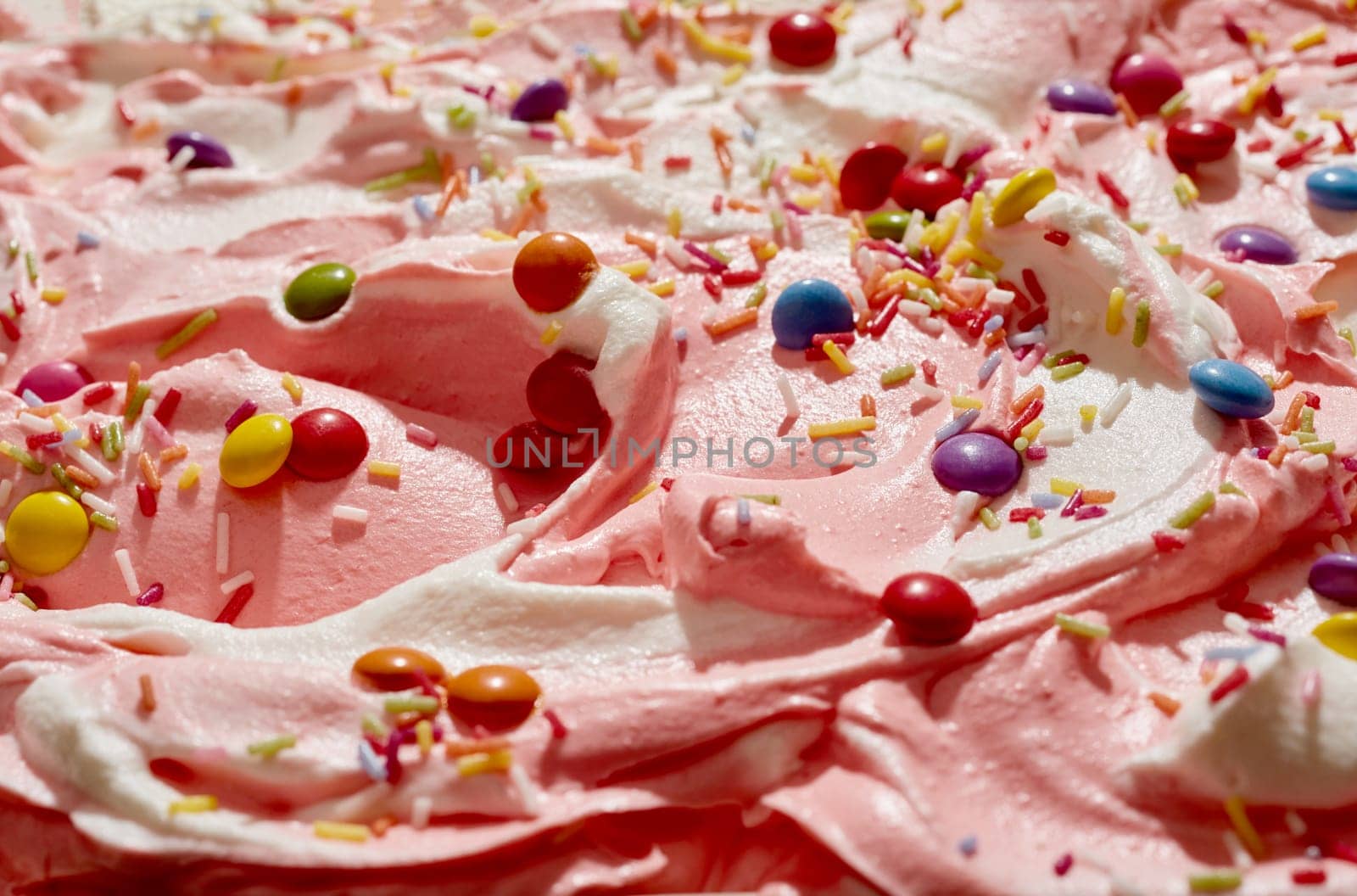 Strawberry and vanilla ice cream topped with sugar-coated chocolate candy and colorful sprinkles for a kids party celebration in a close up background texture