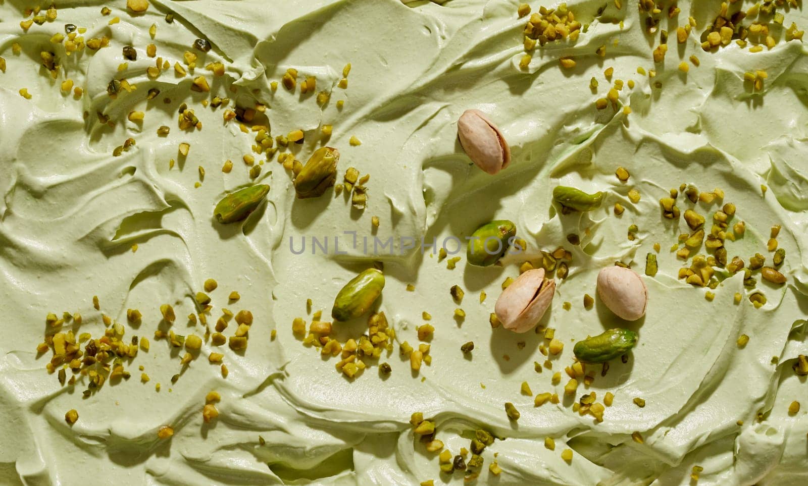 Artisanal homemade green pistachio ice cream with fresh nuts whole, in shells and chopped sprinkled on the surface of the dessert in a full frame background texture