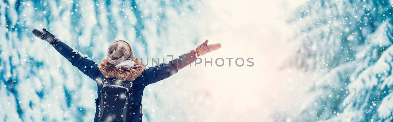 Happy woman with hands up standing in the snowy forest in snowfall. Concept of vacation and holidays.