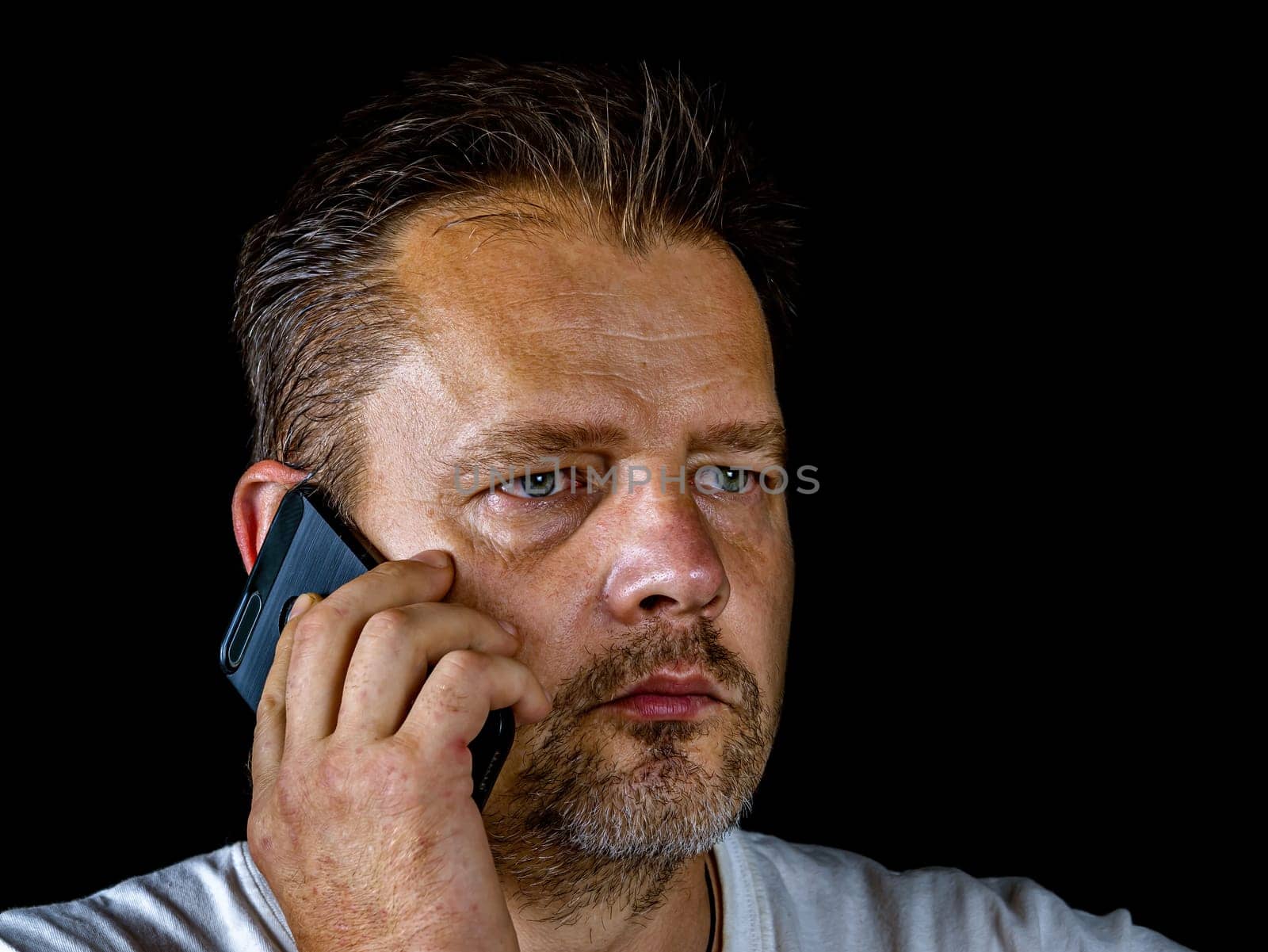 A middle-aged man with a gray beard is talking on a cell phone. Smartphone. Mobile phone. Adult. Cellular. Man's face. Modern technologies. Beard and mustache.