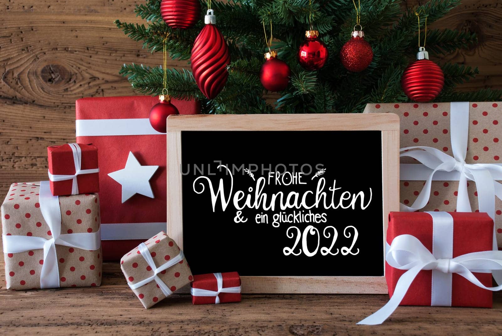 Blackboard With German Text Frohe Weihnachten Und Ein Glueckliches 2022 Means Merry Christmas And A Happy 2022. Christmas Tree With Decoration Like Ball, Gifts And Presents